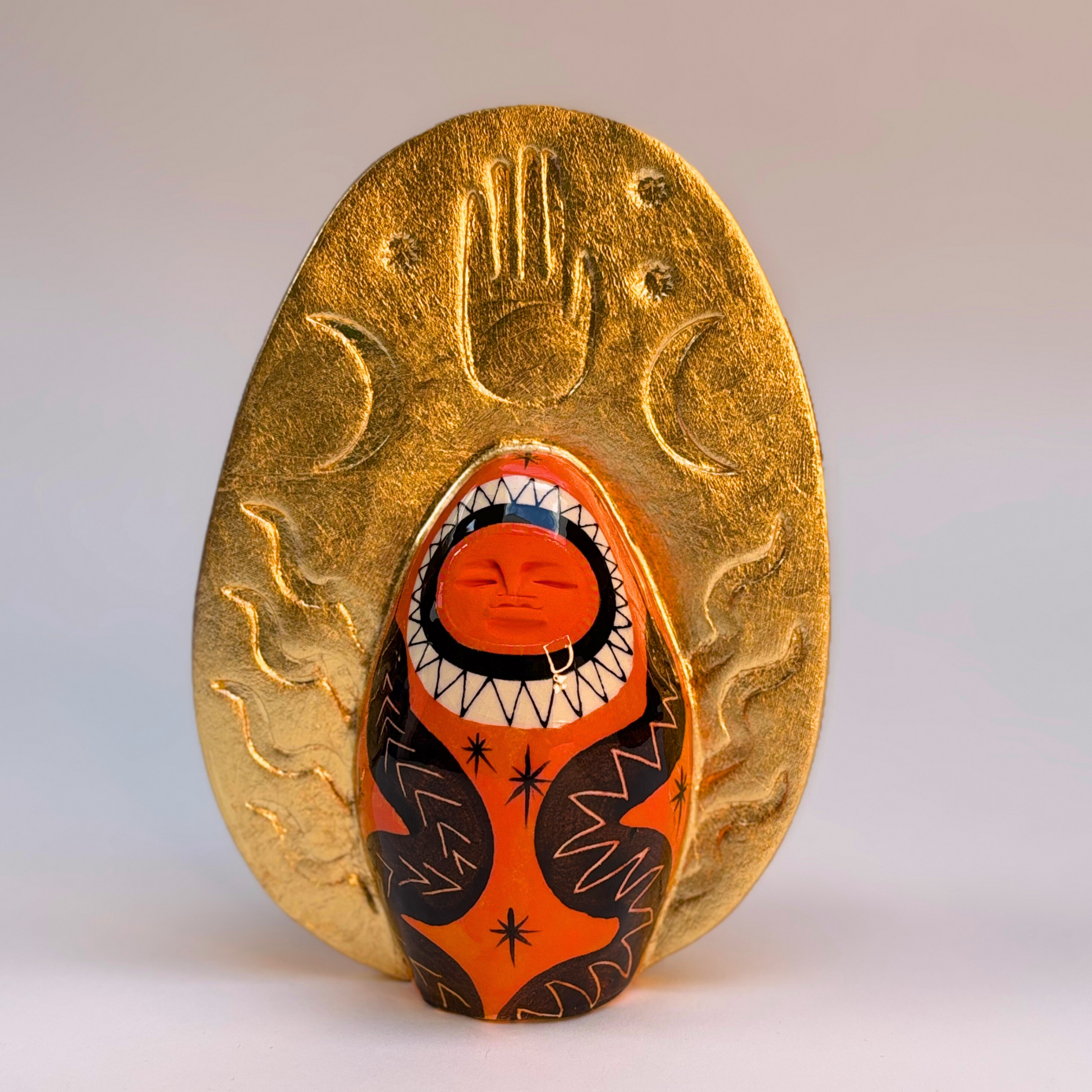 front view of Deep coral ceramic goddess with black snakes and gold crown with hand and moons