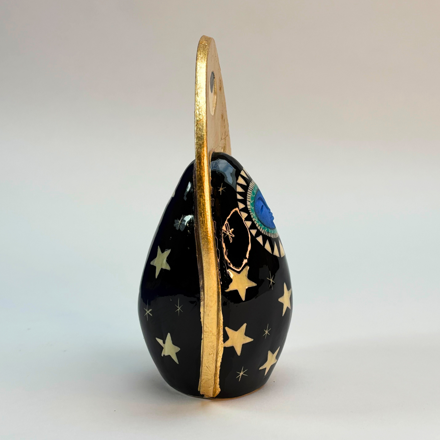 side on view of ceramic goddess black ground hand painted black with white stars and gold crown surround